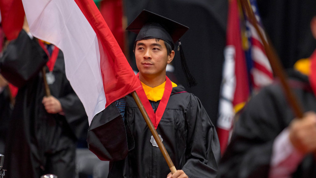 international student carrying a flag of his country at graduation
