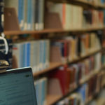 Paige Butler poses with her laptop in the library in front of the bookshelves