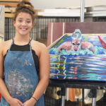 A photo of Jessi Snover standing in front of three paintings of swimmers