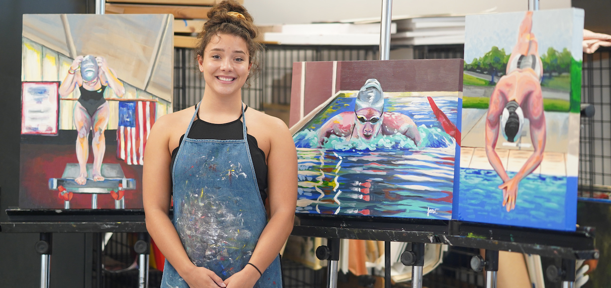 A photo of Jessi Snover standing in front of three paintings of swimmers