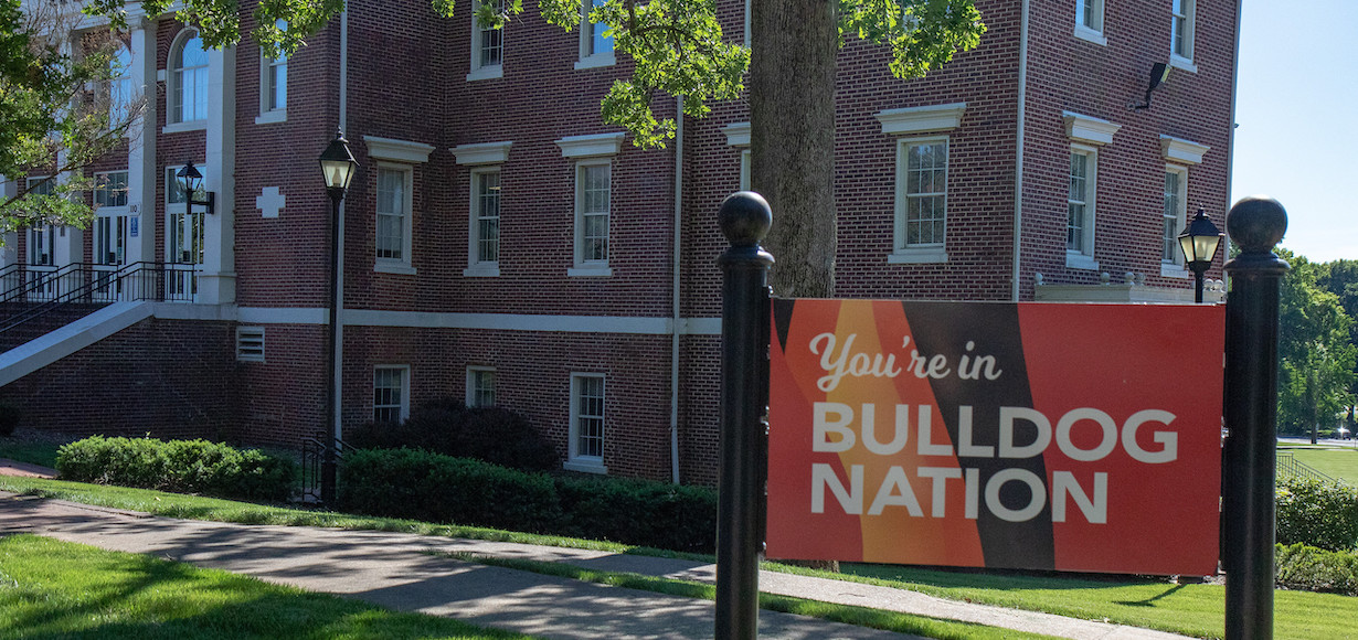A photo featuring the red and black sign that reads you are entering Bulldog Nation. It is in front of Hamrick Hall.