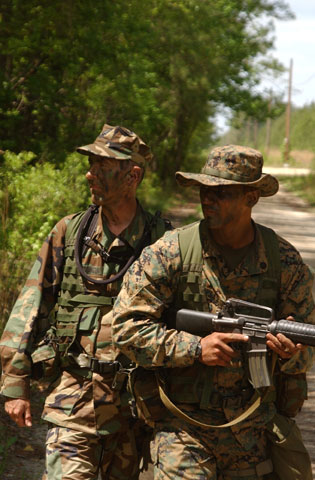 a photo of Terry Eddinger made during Marine Training. He is walking with a body guard. They are wearing Camouflage and the body guard is carrying a gun.