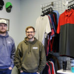 Cam, left, and Bryton Mitchell are brothers and GWU alumni who recently started their own business. They are posing in their shop, with shirts and hats and other items that people can have personalized.