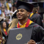 male student taking a photo at 2017 graduation, amidst the crowd, holding his diploma