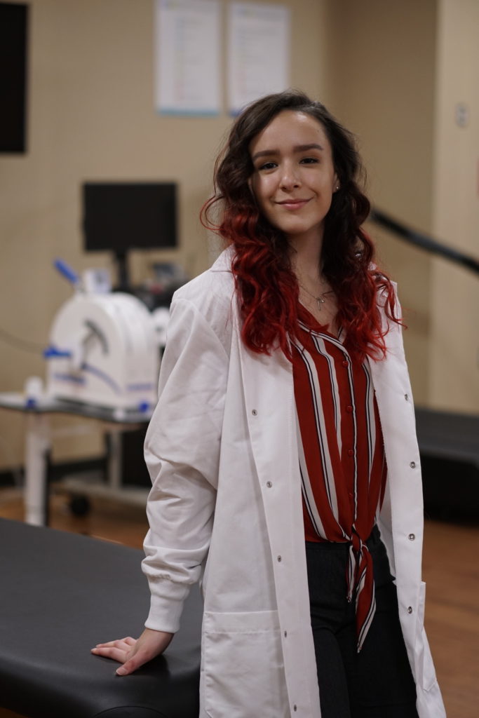Caitie Mayo poses in the exercise science lab at GWU wearing a white lab coat