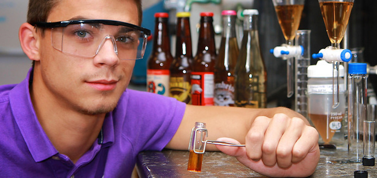 a photo of Jeremy Griffin when he was working in the lab at Gardner-Webb. He is holding a test tube and there are bottles of ginger ale in the background