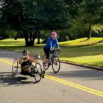 Jacob Conley rides a handcycle and Dr. Shea Stuart rides a bicycle at Cowpens Battleground.
