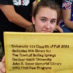 A student holds up a sign for the Little Free Library Box