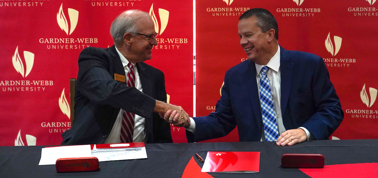 Dr. Marc Stout, left, head of Gaston Christian School, and Dr. William Downs, GWU president, shake hands after signing the agreement