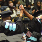 two grads clasp hands above the rows of graduates