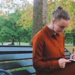 Sarah Goode sits on a park bench reading from a notebook