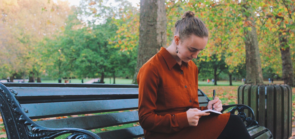 Sarah Goode sits on a park bench reading from a notebook