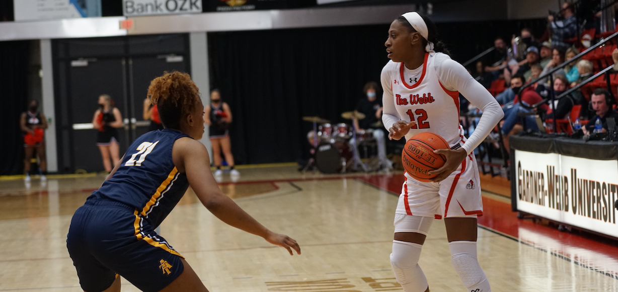 A Gardner-Webb women's baskeball player holds the ball while a person from the other team plays defense.