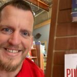 Court Greene poses with his book on a shelf in a bookstore.