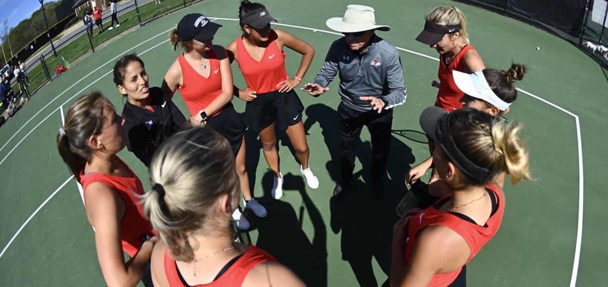The women's tennis team gets directions from the coach on the court