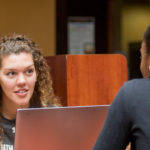 Two female students talking with a computer between them