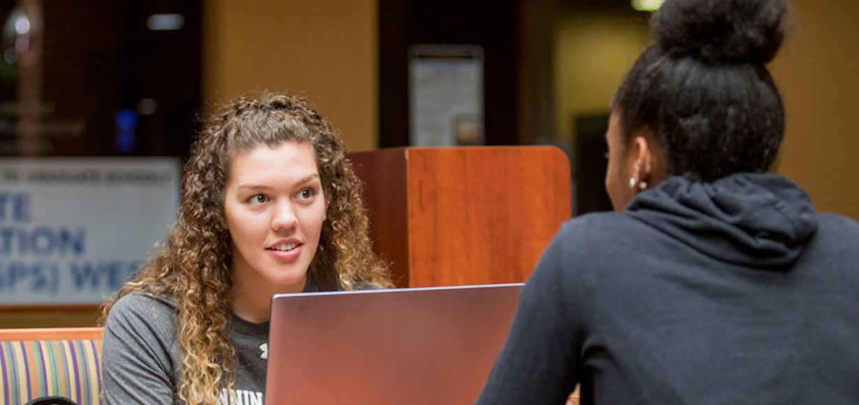 Two female students talking with a computer between them