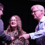 A student is presented an award by two professors.