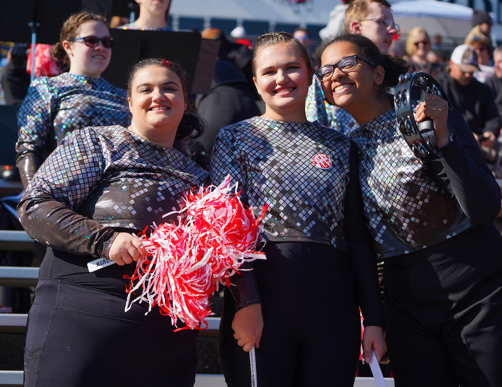 Three members of the band cheer in the stadium seating at a football game. 