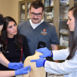 Ashley Kernicky, right, instructs three students on giving shoulder injections.