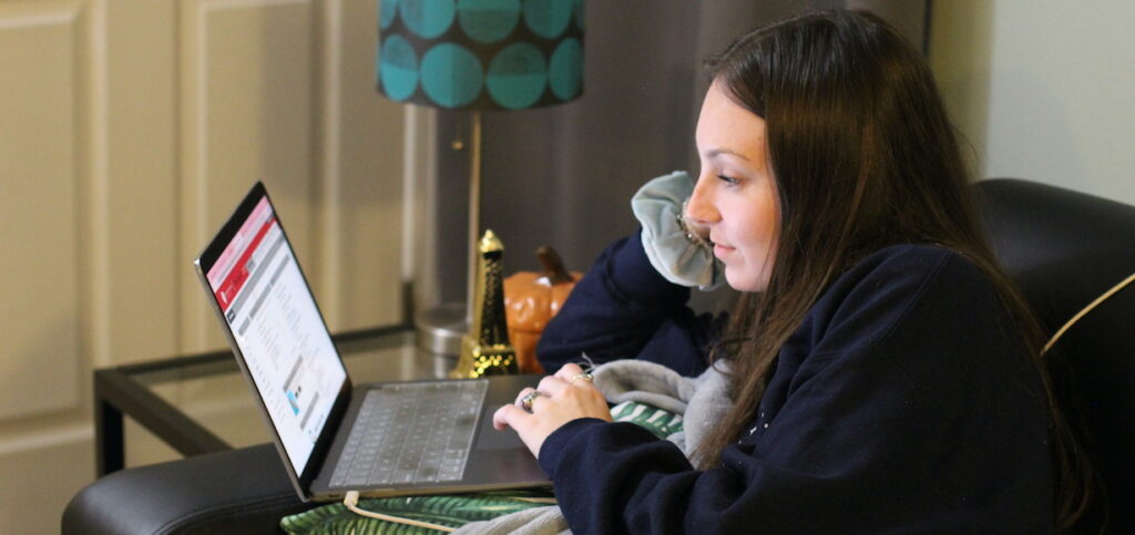 a student sits at a computer in her living room