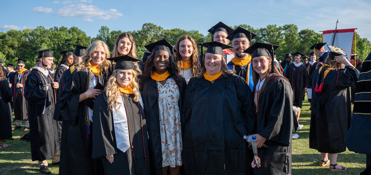 A group of graduates wearing caps and gowns wait for commencement to begin