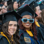 Two graduates smile at the camera during commencement in Spangler Stadium